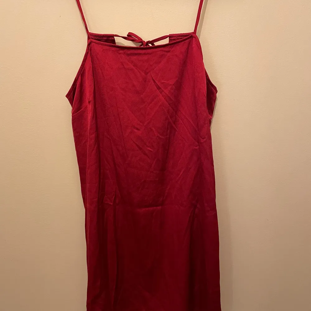 Röd klänning i silkigt material. Öppen rygg med fina knytband. Lite lös i modellen.  Minns ej var den är inköpt ifrån. . Klänningar.