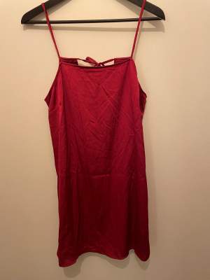 Röd klänning i silkigt material. Öppen rygg med fina knytband. Lite lös i modellen.  Minns ej var den är inköpt ifrån. 