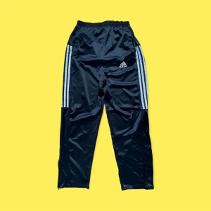 Vintage Loosefit svarta Adidas byxor - Snygga loosefit Adidas polyester byxor, vintage och köpte från Storbritannien. I fint skick, blixtlås vid benen, i gott skick. Passar för en person som är 175-185 cm lång. Ifall högmidjat passar dem för 165-175 cm. För fler bilder eller mått kontakta mig💫