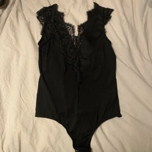 Svart v-ringad body i spets - Säljer en svart v-ringad body, både bak och fram. Stringmodell med spetsdetaljer. Fint skick. Från Pices i storlek medium. 