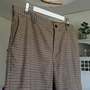 Rutiga kostymbyxor - Rutiga kostymbyxor i svart, vit, brunt och beiget. Slim fit. Stora fram- och bakfickor. Resår och hyllsor i midjan. I nyskick. Strl XL. 