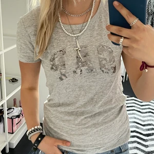 GAP t-shirt med silvrigt tryck - Ljusgrå t-shirt från GAP med silvrigt tryck. Passar XS-M.