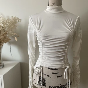 🦢Vit långärmad topp 🦢 - Långärmad topp med fina skrunch detaljer som man kan justera själv med snörena. Väldigt stretchigt material! Jag är en S men kunde ha den i M!  Använd några gånger, men i väldigt fint skick!