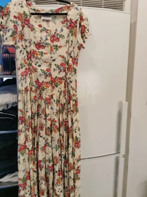 Klänning  - Blommig klänning lång begagnat skick. Behöver strykas men annars inga fel på varan. Knappar hela vägen ner. 