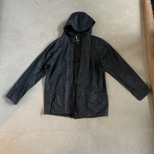 Rains regnjacka - Rains regnjacka i marinblå. Storlek S/M, vilket motsvarar M. Sällan använd. Inga skador, lite skryklig eftersom den inte vart upphängd. Jag är 185cm lång.