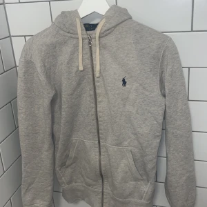 Ralph Lauren zip hoodie - Grå ralph lauren zip hoodie till salu, använd men i gott skick, Litet hål på underarmen. Strl S