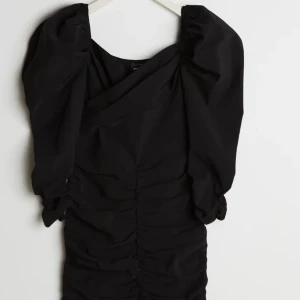 Rynkad klänning med puffärmar strl 42  - Svart, rynkad klänning med puffärmar i storlek 42! Aldrig använd, men väldigt fin och bekväm när jag provat den. Tyvärr hann den aldrig passa mig innan den blev för liten 🥰 Köpt för 599kr men jag säljer för 200kr. Finns i Kungsbacka, men kan också postas. Då ligger frakten på 66kr och köparen står för den. 