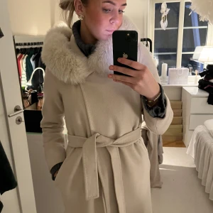 Kappa - Hollies Lucinda kappa som är använd en höst. Fint skick, finns bara en fläck på snörets kant. Ljus beige/ljus rosa färg. Avtagbar päls. Köpt för 6400kr
