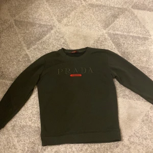 PRADA  - Jag säljer nu en jätte fin Prada tröja, i perfekt skick utan några skador använd 3-4 gånger, den har en jätte fin nyans av grön! Fin på tjej och kille men den är till killar egentligen men den är lika fin på tjejer oxå. Vi kan diskutera ett bra pris. 