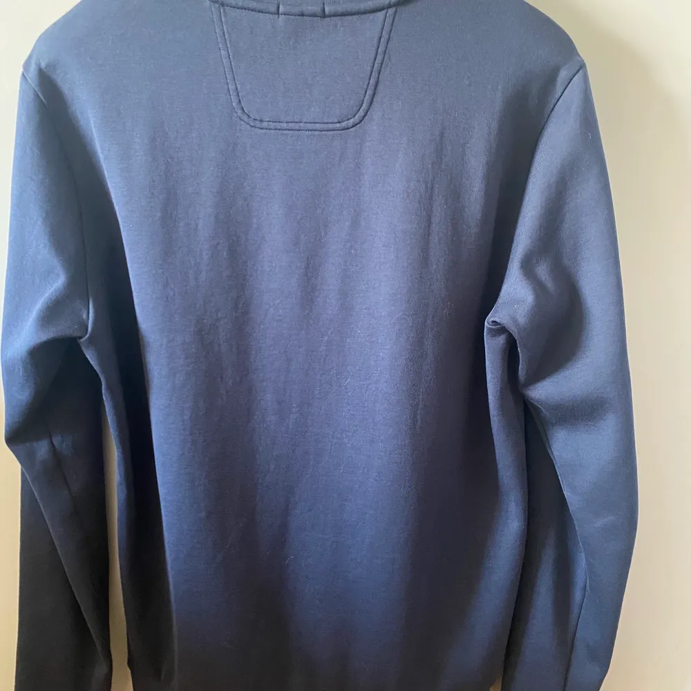 Hugo Boss blå sweatshirt, plagget är i slim fit men sitter som en klassisk sweatshirt. Produkten är använd ett fåtal gånger, men är i väldigt bra skick nästan nyskick.  Det finns inga skador eller defekter. . Tröjor & Koftor.