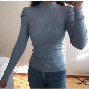 Ribbad mörkare pastellblå tröja, ganska lång ( jag är ungefär 163cm ), sitter relativt tajt med väldigt fin detalj av rynkning i axlarna. Inte tjock i materialet men kan vara ganska varm.