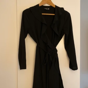 Svart omlottklänning S - Svart omlottklänning med volang som knyts i midjan. Sitter fint på! Tyvärr lite för liten för mig. Storlek XS-S. Bra skick.