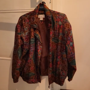 Retrojacka storlek M - Tunn färgsprakande retrojacka i storlek M. Passar bra under vår, sommar eller sensommar/höst. Både knappar och dragkedja.