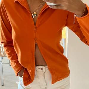 En supersnygg orange tröja köpt second hand från Humana. Tröjan har en dragkedja som kan förslutas både upp- och nedifrån vilket gör att den antingen kan stängas helt eller lämnas öppen. Plagget kan även tajtas till nedtill. Passar de med storlek XS/S