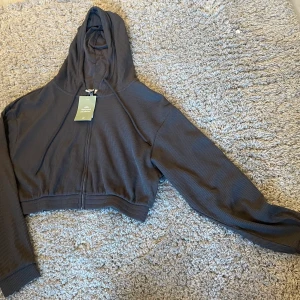 Kort munkjacka strl S. Helt ny med lapp kvar. Mörkgrå  - Kort munjacka/tröja med luva från H&M. Mörkgrå, våfflat mönster strl S. 