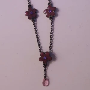 halsband med lila blommor - Fint halsband med mörk kedja, lila blommor. Från tidigt 2000-tal. Köpt på plick. Kan alternativt skicka som brev för 15 kr. 