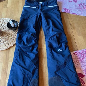 J. Lindeberg skidbyxor - As snygga skidbyxor från j. Lindberg. 2 fickor fram, 2 bak, en på sidan. Lite ”bootcut” känsla. Fodrade, 2 dragkedjor på insida ben om man vill ventilera. Knappt använda, inga skavanker. Goretex. Modell Tracy Ski Pant . Nypris 3495kr. Kan skicka fler bild