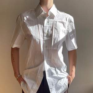 Kortarmad vit skjorta med knappar och krage från Acne. Skjortan har en rak passform och det går lätt att bli av med det skrynkliga genom strykning eller steamning. Plagget är i fint skick. Storlek medium men är oversized och funkar bra på en small eller large. Säljer vidare för 550Kr. 