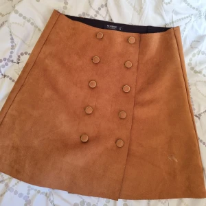 Minikjol i mocka - Minikjol i mocka material med fina gulddetaljerade knappar. I fint skick generellt men har en liten defekt (se bild 3 för close up) pris kan såkalart diskuteras! 😊