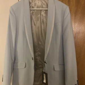 Ljusblå kavaj - Ljusblå kavaj i nyskick. Aldrig använd. Prislapp kvar. Perfekt till studenten/bal!