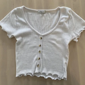 Vit topp - Fin vit croppad topp. Knapparna går ej att knäppa upp.   Sparsamt använd, bra skick!   Står tyvärr inte storlek men skulle säga att den passar XS och S då den är stretchig. 