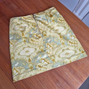 Retrokjol med otroligt mönster! - Mönstrad retrokjol i A-linjemodell. Hög i midjan och kort i modellen. Dragkedja framtill.  Med gul i tonen än första bilden återger.   Midjemått, mätt tvörs över: cirka 38,5 cm. Uppskattas passa en stl 38/M Vintage! 