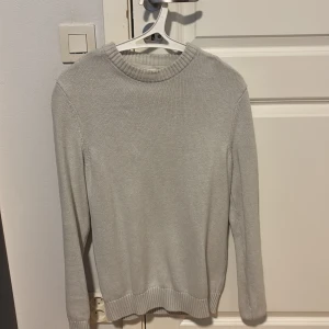 Beige stickad tröja från Dobber - Säljer en stilren beige stickad tröja från Dobber. Tröjan har rund halsringning med bred ribbad kant och ribbade muddar vid ärmslut och nederkant. Perfekt för lager-på-lager och enkel att matcha med jeans eller kjol.