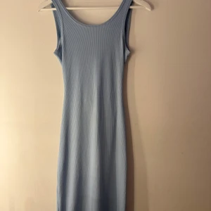 Ljusblå klänning  - Ljusblå ribbstickad klänning med smala axelband och en åtsittande passform. Klänningen har en utskärning i ryggen och en slits på sidan. Strolek S