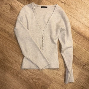 Beige tröja Gina Tricot - Ljusgrå långärmad topp från Gina Tricot med djup v-ringning och dekorativa knappar framtill. Strl: XS. Använd fåtal gånger