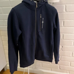 Mörkblå hoodiejacka Sail Racing - Mörkblå hoodiejacka från Sail Racing med dragkedja framtill och bröstficka med logga. Jackan har huva med snörning och är tillverkad i mjuk bomullsmix. Perfekt för dig som gillar sportig och clean stil. Bara att skriva om du har frågor!! 3 små fläckar, syns knappt. Priset kan såklart diskuteras.