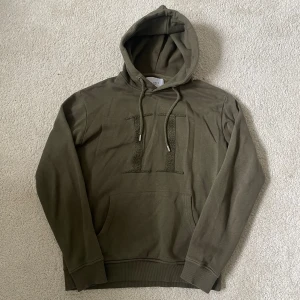 Olivgrön hoodie från Les Deux | M - Snygg olivgrön hoodie från Les Deux med broderad logga framtill. Tröjan har huva med snörning, känguruficka och ribbade muddar. Perfekt för en chill och avslappnad stil.