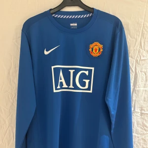 Manchester United Ronaldo blå långärmad tröja - Blå långärmad Manchester United fotbollströja från Nike med Ronaldo 7-tryck på ryggen och AIG som sponsor framtill. Broderat klubbmärke på bröstet och Nike FitDry-material som andas. Perfekt för dig som vill sticka ut på planen eller läktaren.