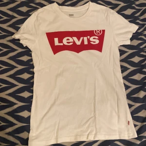 Vit Levi's t-shirt, storlek XXS - Vit t-shirt från Levi's i bomull med klassisk röd logga framtill. Modellen är kortärmad och har en normal passform. Perfekt för dig som gillar en clean och ikonisk streetstil. Unisex i storlek XXS.