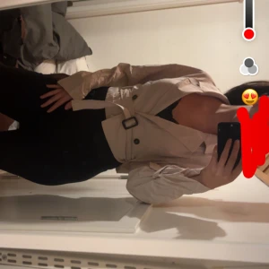 Beige croppad trenchcoat med bälte - Snygg croppad trenchcoat i beige med bälte i midjan och dubbla knappar framtill. Jackan har långa ärmar och klassisk krage, perfekt för dig som vill ha en trendig och stilren look.