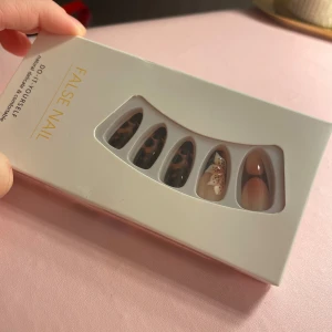 Lösnaglar med leopardmönster och blomma - Snygga lösnaglar i mandelform med trendigt leopardmönster, nude-toner och en nagel dekorerad med en vit blomma. Kommer i förpackning med flera storlekar, nagelfil och klisterlappar. Perfekt för dig som vill ha coola och unika naglar snabbt.