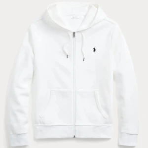 Vit hoodie från Polo Ralph Lauren - Snygg vit hoodie från Polo Ralph Lauren med dragkedja framtill, huva med snörning och klassisk logga broderad på bröstet. Tröjan har känguruficka och är tillverkad i mjuk bomull. Perfekt för en clean och stilren look. Dragit bort snöret så den finns inte. Den är storlek L men passar även M. 