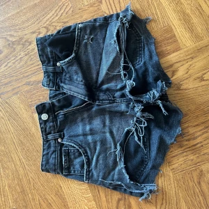 Svarta jeansshorts med fransig kant från Zara - Säljer ett par svarta jeansshorts från Zara i storlek 34. De har hög midja men kan ha de låg midja, rå och fransig kant samt slitna detaljer framtill för en edgy vibe.