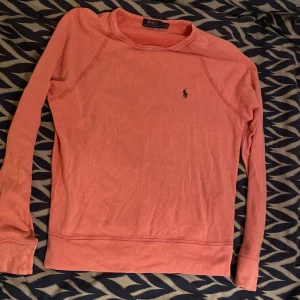 Rosa långärmad tröja Polo Ralph Lauren - Säljer en korallrosa långärmad tröja från Polo Ralph Lauren. Tröjan har klassisk crewneck, broderad marinblå logga på bröstet och är gjord i mjuk bomull. Perfekt för dig som gillar stilren och enkel design. Inga skavanker på varan, näst intill nyskick.