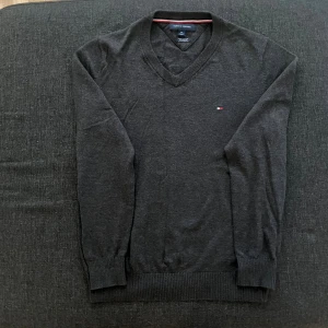 Svart v-ringad tröja Tommy Hilfiger - Klassisk svart v-ringad tröja från Tommy Hilfiger med diskret logga på bröstet. Tröjan har långa ärmar, ribbade muddar och är tillverkad i mjuk bomull. Perfekt för lager-på-lager och stilrena outfits.