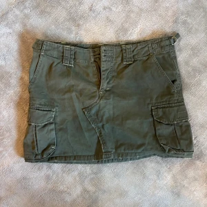 Grön cargokjol med fickor - Snygg grön cargokjol med stora sidofickor och bälteshällor. Kjolen har en kort modell och är tillverkad i bomull, perfekt för en avslappnad och cool stil. Säljs pga för stor.