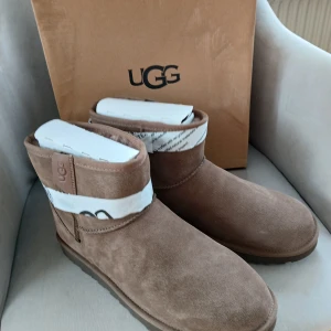 Nya UGG boots strl 43 - Säljer ett par klassiska bruna UGG boots i mjuk mocka med rund tå och platt sula. Skorna har en fluffig insida och UGG-logga bak på hälen. Perfekta för kyliga dagar och riktigt sköna att dra på sig. Snygg och enkel design som funkar till det mesta.