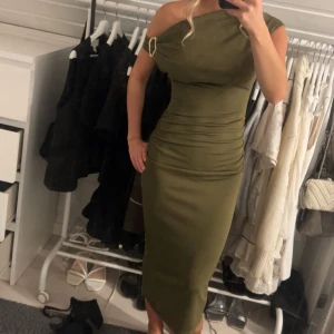 Olivgrön one shoulder långklänning - Snygg olivgrön långklänning och one shoulder med guld detalj. Använd två gånger och inga defekter. Stretchigt material.