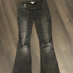 Svarta bootcut jeans Gina Tricot XS - Svarta bootcut jeans från Gina Tricot i storlek XS. Jeansen har slitningar vid knäna, två framfickor med coola detaljer och dubbla knappar i midjan. Materialet är stretchigt jeans och färgen är tvättad svart med lite ljusare partier.
