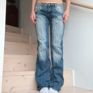 Blå baggy jeans med urtvättningar - Snygga blå jeans med baggy-modell och urtvättade detaljer framtill och baktill. Jeansen har låg midja och klassiska fickor, samt dekorativa paljetter på bakfickorna. Perfekta för en avslappnad och trendig look. INTE MINA BILDER