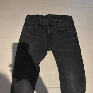 Svarta jeans från Lee - Säljer ett par svarta jeans från Lee med klassisk femficksdesign och raka ben. Jeansen har en mörk tvätt och tydliga sömmar, tillverkade i slitstarkt denimtyg. Perfekta för dig som gillar en enkel och tidlös look.
