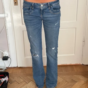 Ltb blå jeans bootcut - Säljer ett par blå ltb jeans med bootcut och låg midja. Jeansen har slitna detaljer och hål på ena benet för en cool, avslappnad look. Klassisk femficksmodell i jeansmaterial med ljus tvätt och vita sömmar. Storlek 28W, 32L