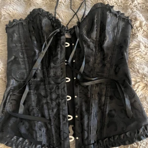 Svart korsett - Svart korsett perfekt till halloween🎃 Endats använd en gång, köpt på sekondhand så vet tyvärr inte vart den är ifrån. Det står storlek M men är väldigt lätt att justera, passar mig som är xs/s.   Har ett litet hål som visas på sista bilden, men det är inget som syns när den sitter på. Vid önskemål så kan jag sy igen det. Pris går att diskutera🤍