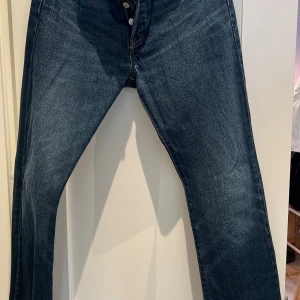 Levi's 501 Premium jeans blå W30 L34 - Klassiska Levi's 501 Premium jeans i mörkblå denim med raka ben och knäppning fram. Snygga kontrastsömmar och ikonisk läderpatch bak. Perfekta för dig som gillar tidlös stil och vill ha ett par jeans som alltid funkar.