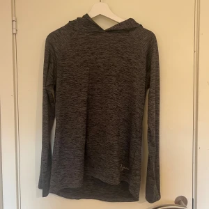 Mörkgrå hoodie från Ullared  - Mörkgrå melerad hoodie från Ullared med lång ärm, huva och praktisk ficka med dragkedja på ryggen. Tillverkad i mjukt och lätt syntetmaterial, perfekt för träning eller chill. Reflekterande detalj baktill för extra synlighet.