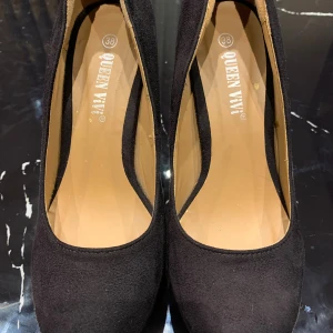 Svarta pumps från Queen Vivi, storlek 38 - Snygga svarta pumps från Queen Vivi i storlek 38. Skorna har hög klack och plattform, är klädda i mockaliknande material och har en klassisk rund tå. Perfekta för dig som vill ha en stilren och elegant look.